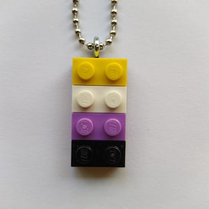 Peut inclure: Un collier avec un pendentif composé de quatre briques LEGO empilées. Les briques sont jaunes, blanches, violettes et noires. Le logo LEGO est visible sur chaque brique.