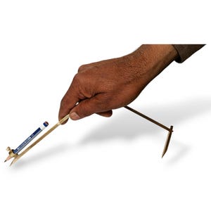 Peut inclure: Une boussole faite à la main en bois et en laiton, avec un crayon et un petit tube de peinture bleue et blanche. La boussole est tenue par une main sur fond blanc.