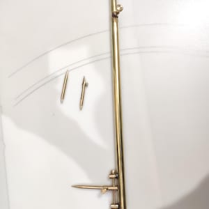 May include: A brass compass with a long arm and a shorter arm with a sharp point. The compass is on a white surface with two smaller brass compasses.