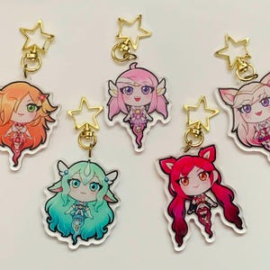 May include: Five colourful character keychains featuring anime-style girls with different hair colours and outfits. Each keychain has a gold star charm attached to a gold ring.