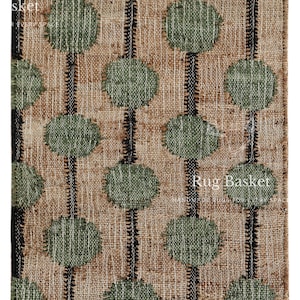 Op de afbeelding: Een rechthoekig tapijt met een beige achtergrond, met verticale zwarte strepen en olijfgroene cirkelvormige patronen. Het tapijt heeft een gefranjerde rand en de tekst "Rug Basket".
