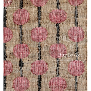 Op de afbeelding: Rechthoekig vloerkleed met een natuurlijke jute achtergrond. Het vloerkleed heeft een patroon van roze cirkels verbonden door zwarte verticale lijnen. De randen zijn afgewerkt met een franje. De tekst "Rug Basket" is zichtbaar.