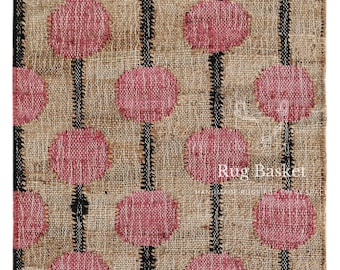 Puede incluir: Alfombra rectangular con fondo de yute natural. La alfombra presenta un patrón de círculos rosas conectados por líneas verticales negras. Los bordes están acabados con flecos. El texto "Rug Basket" es visible.