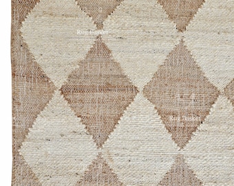 May include: A close-up of a woven jute rug with a diamond pattern. The diamonds alternate between natural beige and light brown. The rug has a fringe along the bottom edge. The rug is a neutral color and would fit in any room.