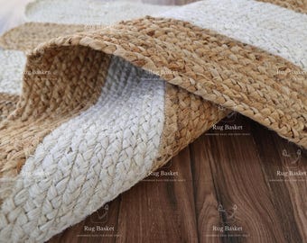 May include: A close-up of a natural fiber rug with a white and natural jute striped pattern. The rug is made of woven jute and has a natural, earthy look.