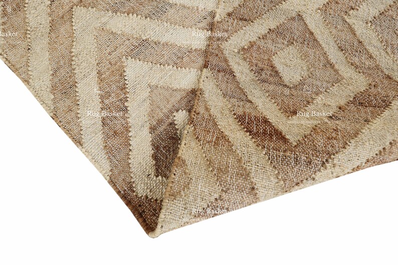 May include: Close-up of a beige and brown geometric patterned rug. The rug features a repeating diamond and stripe design, with varying shades of beige and brown. The rug is made of a woven material.