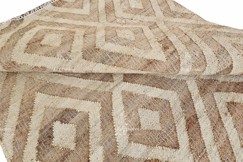 May include: A natural fiber rug with a geometric diamond pattern in shades of beige and brown. The rug is folded over, showcasing the texture and design. The rug is suitable for home decor.