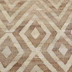 May include: Close-up of a woven rug with a geometric diamond pattern. The rug features alternating shades of beige and brown, creating a textured, neutral design. The repeating pattern gives the rug a modern, yet rustic feel.