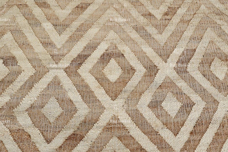 May include: Close-up of a woven rug with a geometric diamond pattern. The rug features alternating shades of beige and brown, creating a textured, neutral design. The repeating pattern gives the rug a modern, yet rustic feel.