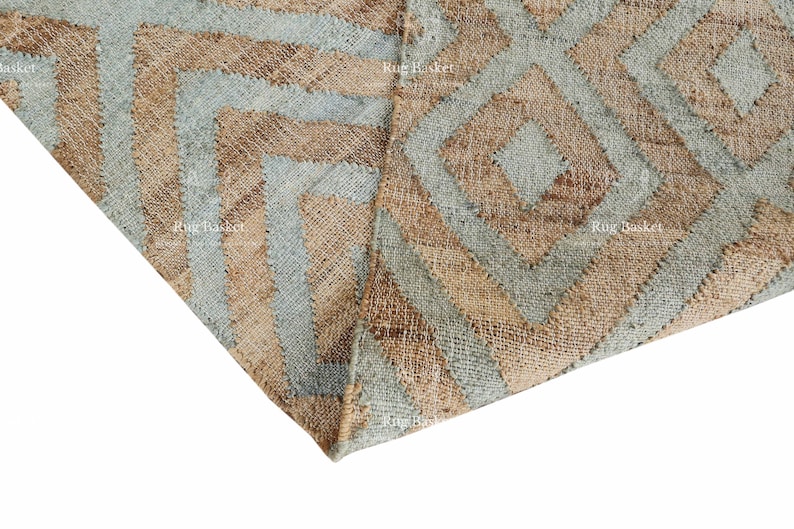 Pu&ograve; includere: Primo piano di un tappeto tessuto con un motivo geometrico. Il tappeto presenta un motivo ripetuto di diamanti e chevron nelle tonalit&agrave; del beige e dell'azzurro. La trama del tappeto &egrave; visibile, suggerendo una costruzione in fibra naturale.