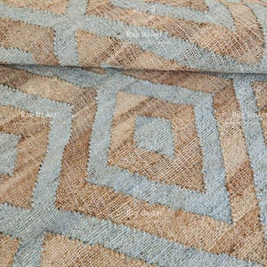 Pu&ograve; includere: Primo piano di un tessuto intrecciato con un motivo geometrico. Il design presenta forme e linee a diamante azzurre e marroni. Il tessuto ha un aspetto strutturato e naturale, che suggerisce un tappeto o un tessuto decorativo.