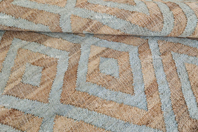 Pu&ograve; includere: Primo piano di un tessuto intrecciato con un motivo geometrico. Il design presenta forme e linee a diamante azzurre e marroni. Il tessuto ha un aspetto strutturato e naturale, che suggerisce un tappeto o un tessuto decorativo.