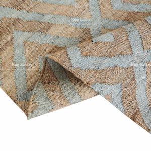Pu&ograve; includere: Un tappeto tessuto con un motivo geometrico. Il tappeto presenta fasce alternate di blu chiaro e beige, creando un design a zig-zag. Il tappeto &egrave; realizzato in un materiale strutturato.