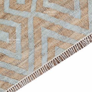 Pu&ograve; includere: Primo piano di un tappeto tessuto con un motivo geometrico. Il tappeto presenta un motivo ripetuto di diamanti e zig-zag azzurri e marroni. Il bordo del tappeto ha una frangia di fili bianchi.