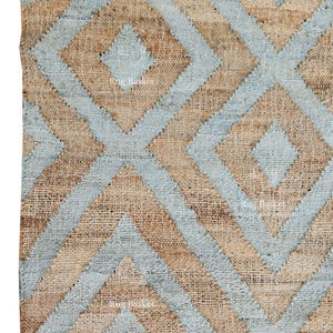Pu&ograve; includere: Primo piano di un tappeto in juta con un motivo geometrico a rombi. Il design presenta rombi blu chiaro e beige alternati. Il tappeto ha un bordo con frange.