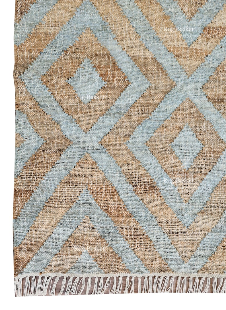 Pu&ograve; includere: Primo piano di un tappeto in juta con un motivo geometrico a rombi. Il design presenta rombi blu chiaro e beige alternati. Il tappeto ha un bordo con frange.