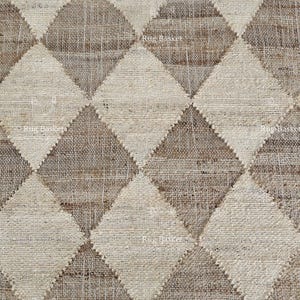 May include: Close-up of a woven rug with a repeating diamond pattern. The diamonds alternate between light beige and a darker, earthy brown. The texture of the rug appears to be coarse and natural, suggesting a handmade or artisanal quality.