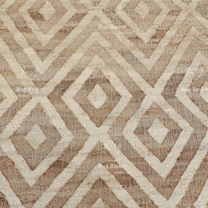 May include: Close-up of a beige and brown geometric patterned rug. The rug features a repeating diamond and zig-zag design. The rug is made of a woven material and has a textured appearance. The rug is suitable for home decor.