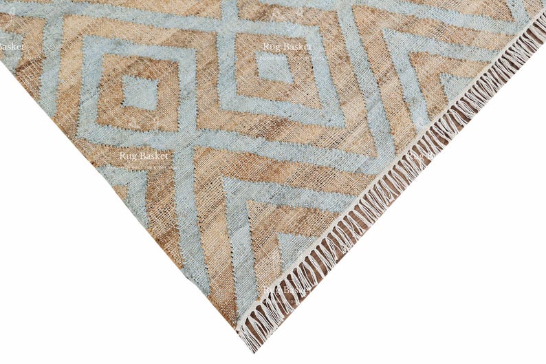 Pu&ograve; includere: Primo piano di un tappeto geometrico con un motivo a rombi. Il tappeto presenta una combinazione di colori azzurro e beige. Il bordo del tappeto ha un dettaglio a frange. Il tappeto &egrave; realizzato in un materiale tessuto.