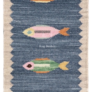 May include: A rectangular runner rug featuring a dark blue center with a jagged edge and a beige border. The rug displays six stylized fish in various colors including yellow, orange, pink, and green, arranged in a vertical row. The text Rug Basket is visible.