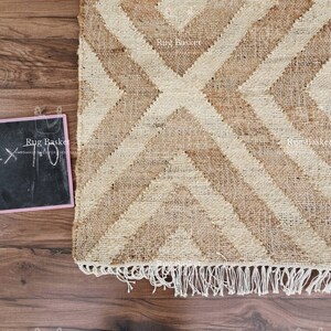 May include: A woven jute rug with a geometric diamond pattern in shades of beige and brown. The rug has a fringed edge and a small chalkboard with the dimensions 5.1 x 7.0 inches.