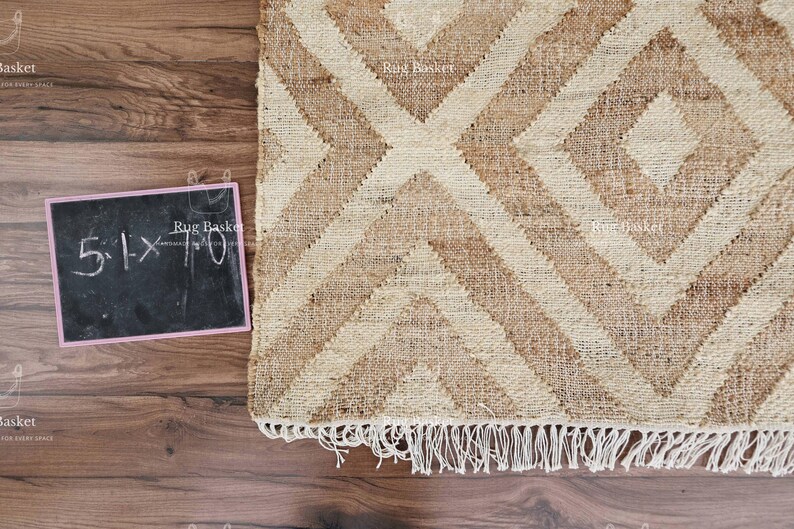 May include: A woven jute rug with a geometric diamond pattern in shades of beige and brown. The rug has a fringed edge and a small chalkboard with the dimensions 5.1 x 7.0 inches.