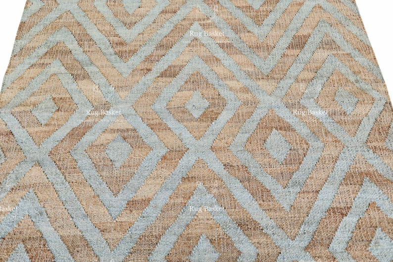Pu&ograve; includere: Primo piano di un tappeto tessuto con un motivo geometrico a rombi. Il tappeto presenta un motivo ripetuto di rombi azzurri e beige. La trama del tappeto &egrave; visibile, suggerendo un materiale in fibra naturale. L'estetica generale &egrave; moderna e neutra.