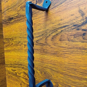 Peut inclure: Poignée de porte en métal noir avec un design torsadé. La poignée est fixée à une surface en bois.