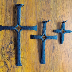 Könnte beinhalten: Drei schwarze Metallkreuze in verschiedenen Größen hängen an einer Holzwand. Das größte Kreuz hat ein sternförmiges Design in der Mitte.