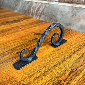 Può includere: Maniglia per porta in metallo nero con un design attorcigliato. La maniglia ha due volute decorative alle estremità.