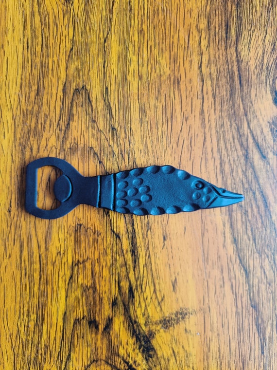 A pair of hand-forged fish-shaped bottle openers — the fish form shows real blacksmithing artistry and makes a dead-useful gift feel genuinely artistic.