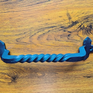 May include: A black metal door handle with a twisted design. The handle has a decorative, pointed end on each side.