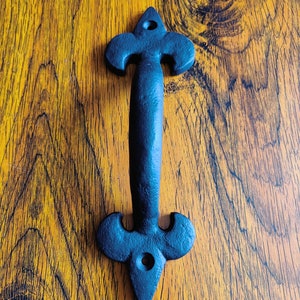 May include: Black cast iron door handle with a fleur-de-lis design.