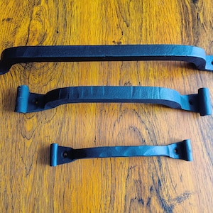 May include: Three black metal door handles of different sizes. The handles are curved and have a simple design.
