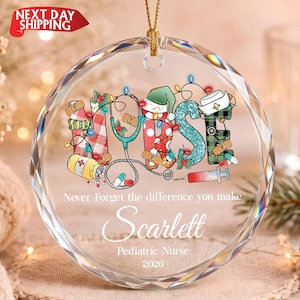 May include: A round, faceted glass ornament featuring the word NURSE in colorful, patterned letters decorated with medical icons like a stethoscope, pills, and a nurse cap. It includes the text Never Forget the difference you make, Scarlett, Pediatric Nurse, 2026.