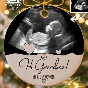 May include: A round ceramic ornament featuring a black and white ultrasound image of a fetus. Below the image, the text reads "Hi Grandma!" in script, followed by "SEE YOU IN OCTOBER! 2025" in block letters. A gold string is attached to the top.