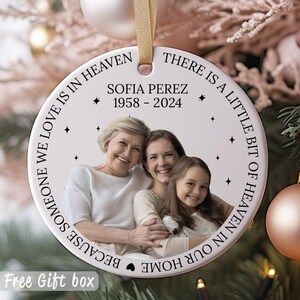 May include: White ceramic ornament with a photo of three people and the text "THERE IS A LITTLE BIT OF HEAVEN IN OUR HOME BECAUSE SOMEONE WE LOVE IS IN HEAVEN SOFIA PEREZ 1958-2024".