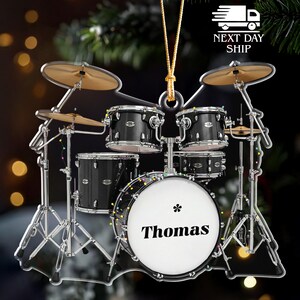 May include: A miniature drum set ornament with a personalized bass drum that reads "Thomas". The black drums have silver hardware and are accented with gold-colored cymbals. The ornament is designed to hang.