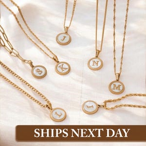 May include: Five gold necklaces with white and gold pendants featuring different letters of the alphabet. The necklaces are displayed on a white fabric background. Ships Next Day.