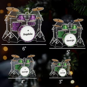 May include: Four acrylic drum set ornaments in purple and green, with the names "Sophia" and "George" on the bass drums. Sizes range from 3 to 6 inches in width.
