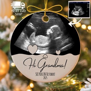 May include: Round ceramic ornament with a sonogram image, black border, and gold string. The ornament says "Hi Grandma! See you in October! 2025" with two heart graphics. A smaller sonogram image is in the upper right corner.