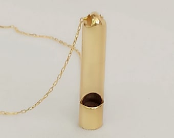 May include: A gold chain necklace with a gold whistle pendant. The whistle is cylindrical in shape with a round opening at the top.
