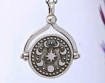 May include: A silver-toned pendant necklace featuring a rotating circular charm. The charm displays a star and crescent moon design. The necklace hangs from a delicate chain against a white background.