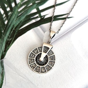 May include: A silver necklace with a spinning zodiac wheel pendant. The wheel is decorated with black stones and the zodiac symbols.