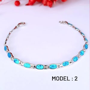May include: Silver-toned bracelet featuring oval, light blue gemstones. The bracelet is composed of interconnected links, with each link holding a gemstone. The text "MODEL : 2" is displayed below the bracelet.