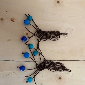May include: A pair of brown macrame earrings with blue and turquoise beads. The earrings are handmade and feature a unique knotted design.