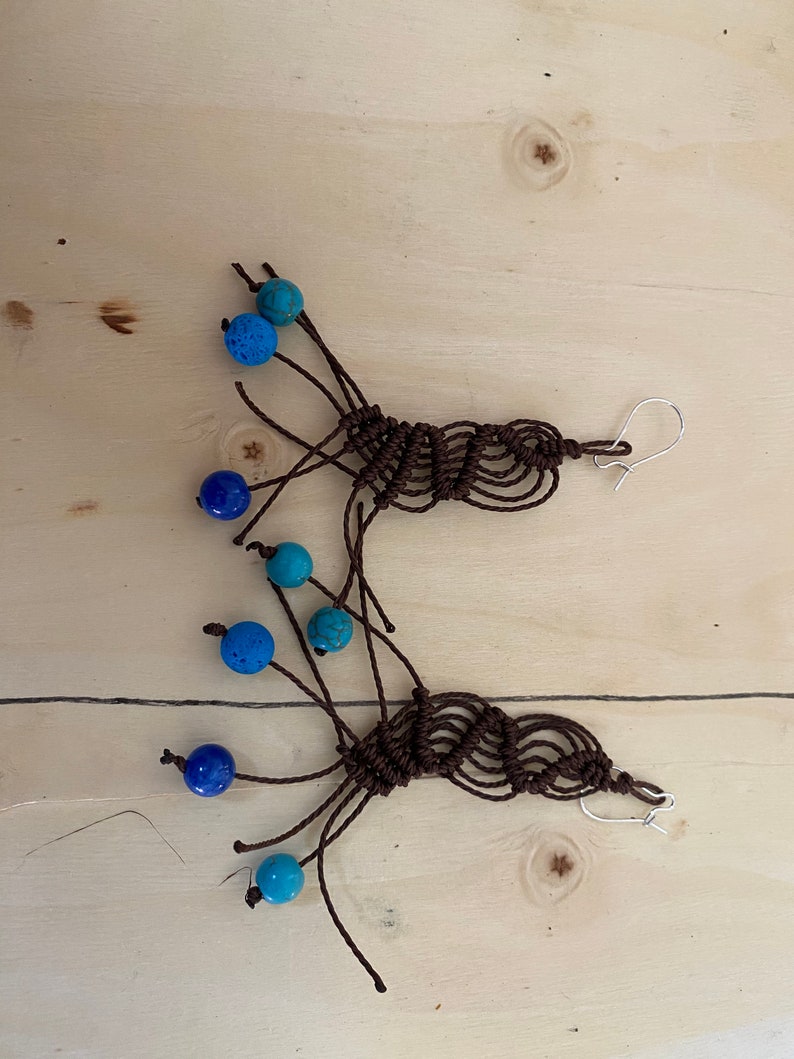 May include: A pair of brown macrame earrings with blue and turquoise beads. The earrings are handmade and feature a unique knotted design.