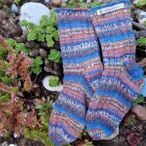 Könnte beinhalten: Ein Paar bunte gestreifte Stricksocken in Blau, Orange, Rosa und Weiß. Die Socken haben ein Etikett mit der Aufschrift "OwlSocksHandmade.com".