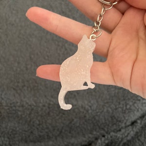 May include: A white glitter cat keychain with a silver chain and ring.