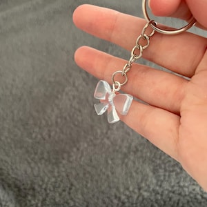 Puede incluir: Un llavero de plástico transparente con forma de lazo con una cadena y un anillo plateados.